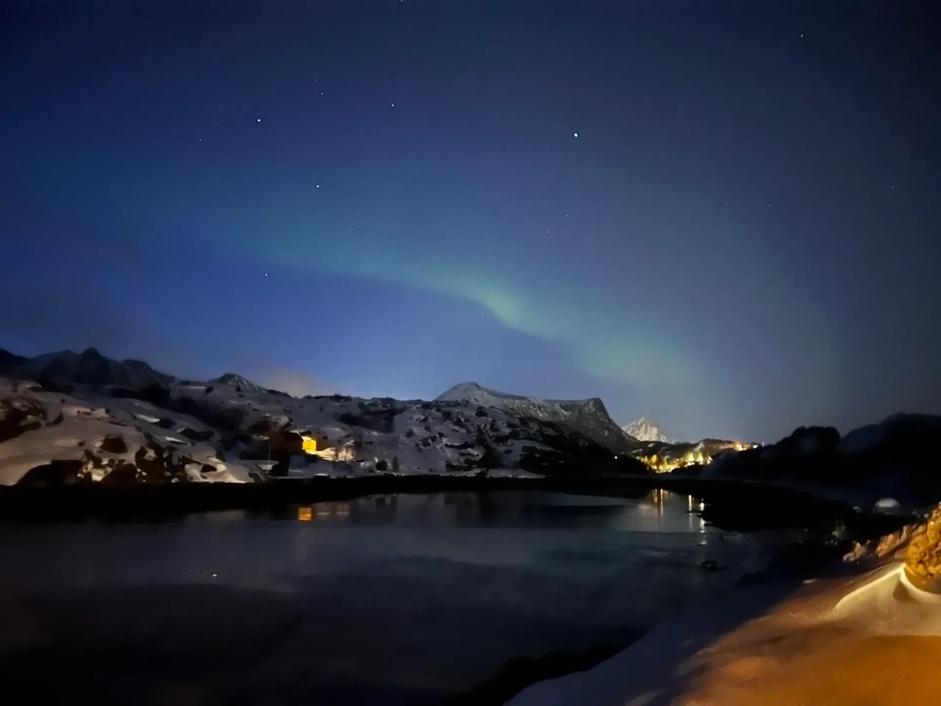 Group of skiers posing on a snowy mountain with lake and peaks behind.