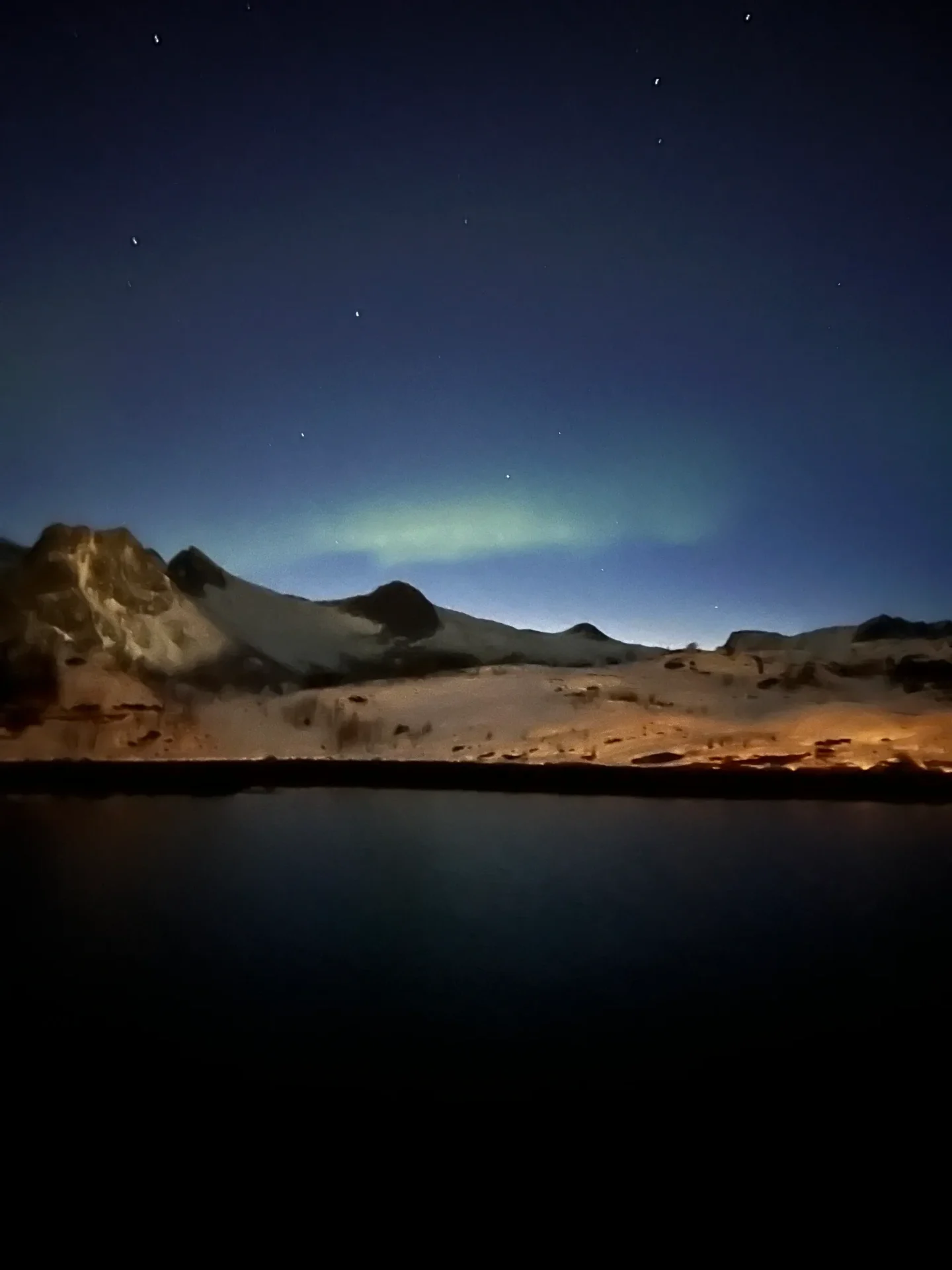 Group of skiers posing on a snowy mountain with lake and peaks behind.