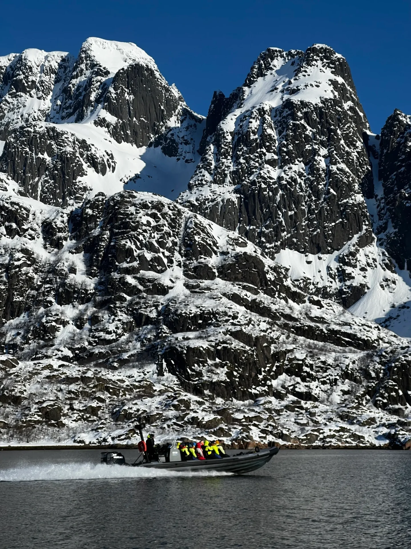 Group of skiers posing on a snowy mountain with lake and peaks behind.