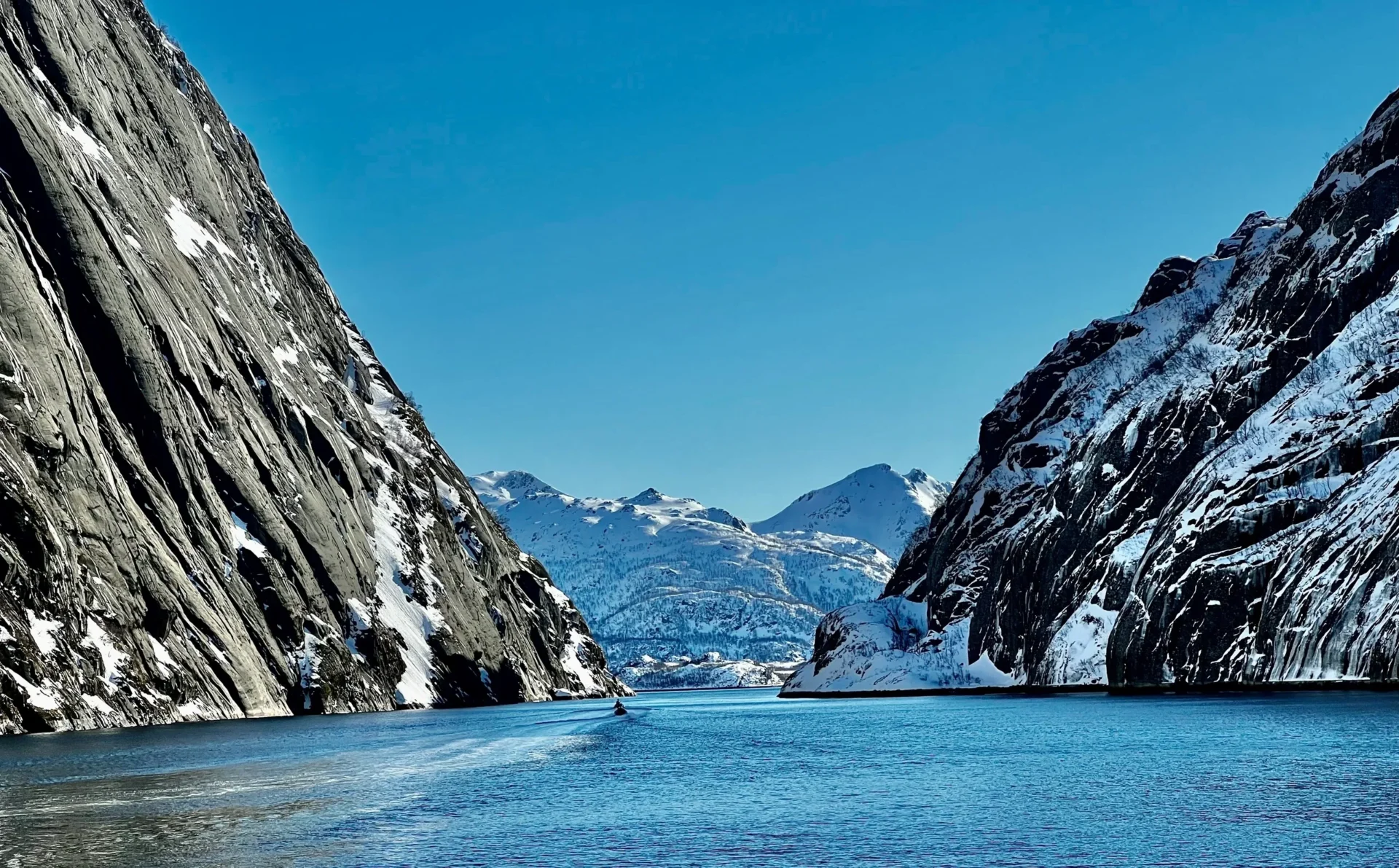 Group of skiers posing on a snowy mountain with lake and peaks behind.