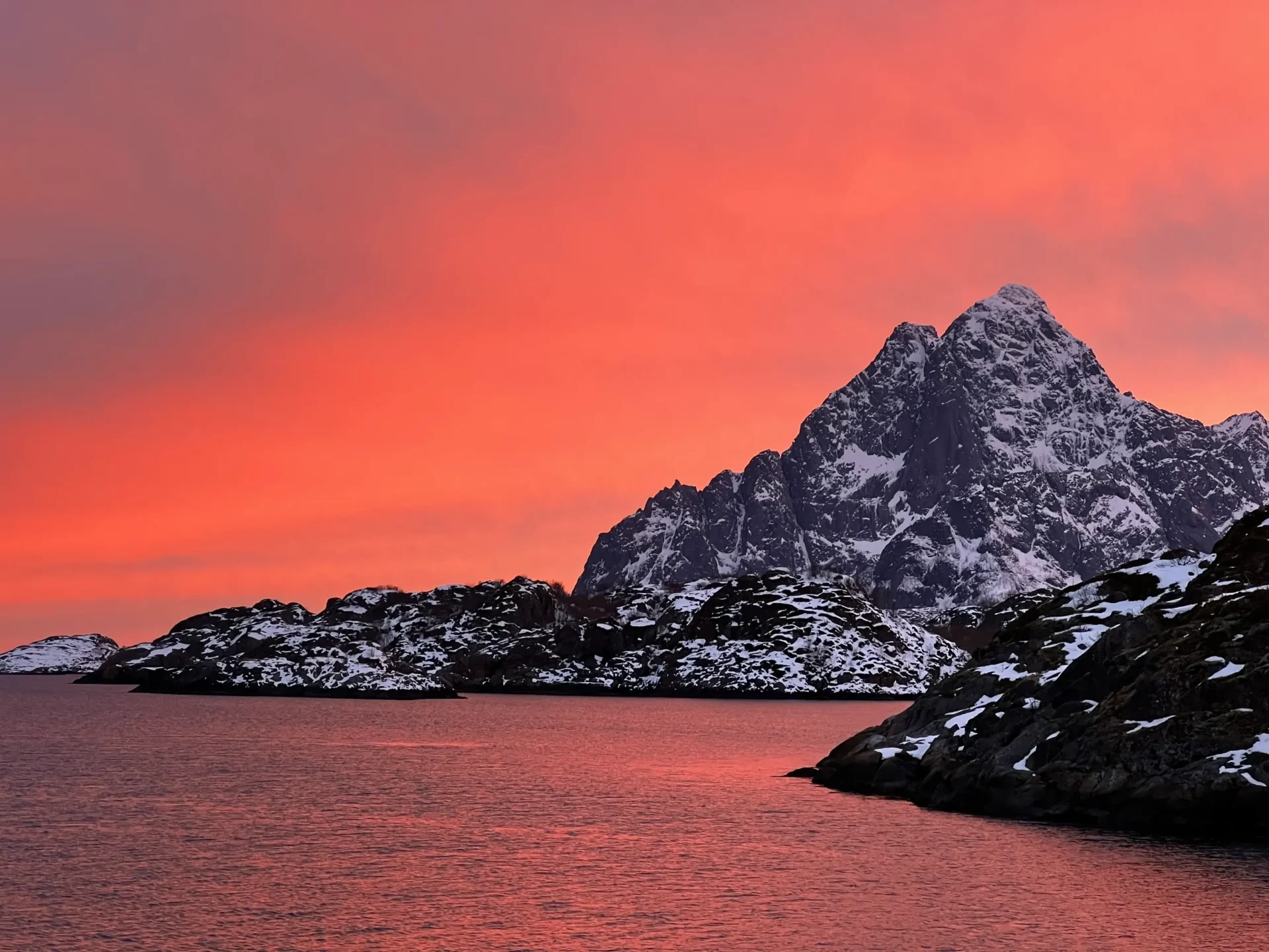 Group of skiers posing on a snowy mountain with lake and peaks behind.