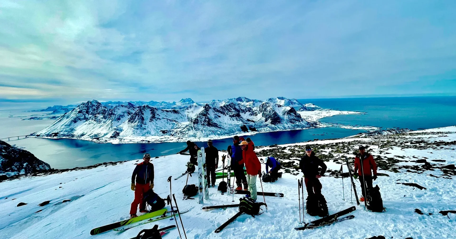 Group of skiers on a snowy mountain with scenic ocean and snowy peaks.