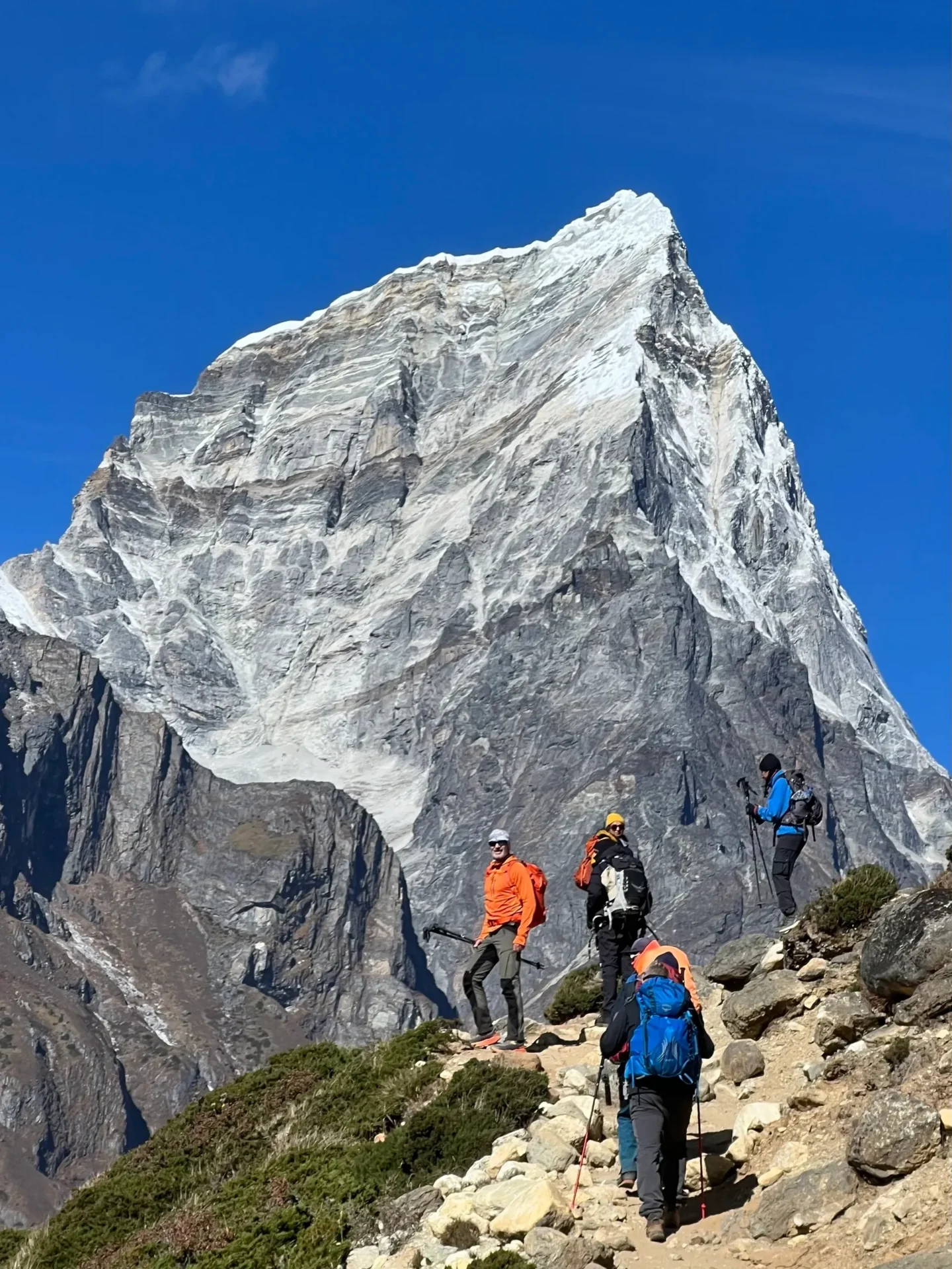 Group of skiers posing on a snowy mountain with lake and peaks behind.