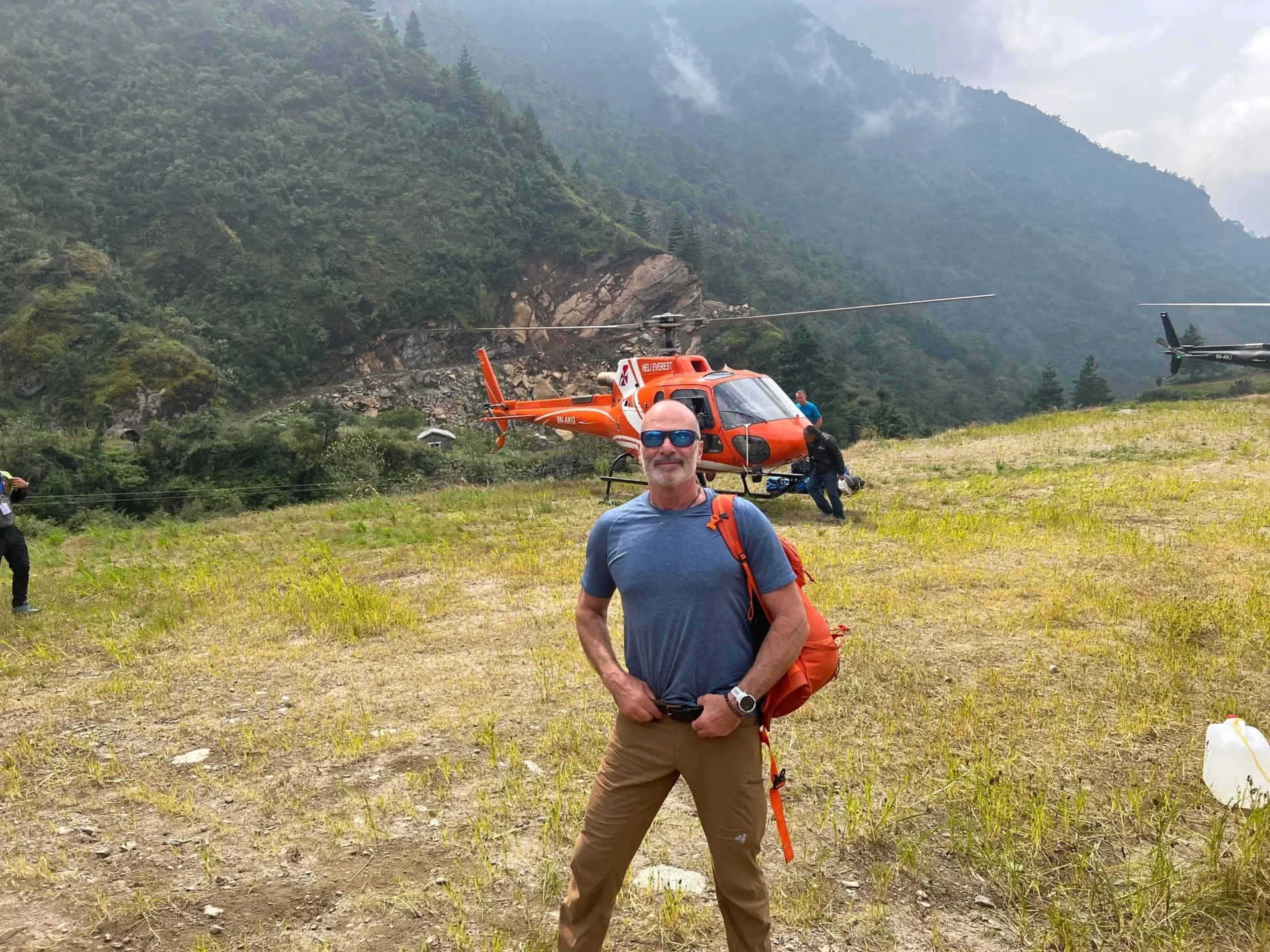 Group of skiers posing on a snowy mountain with lake and peaks behind.