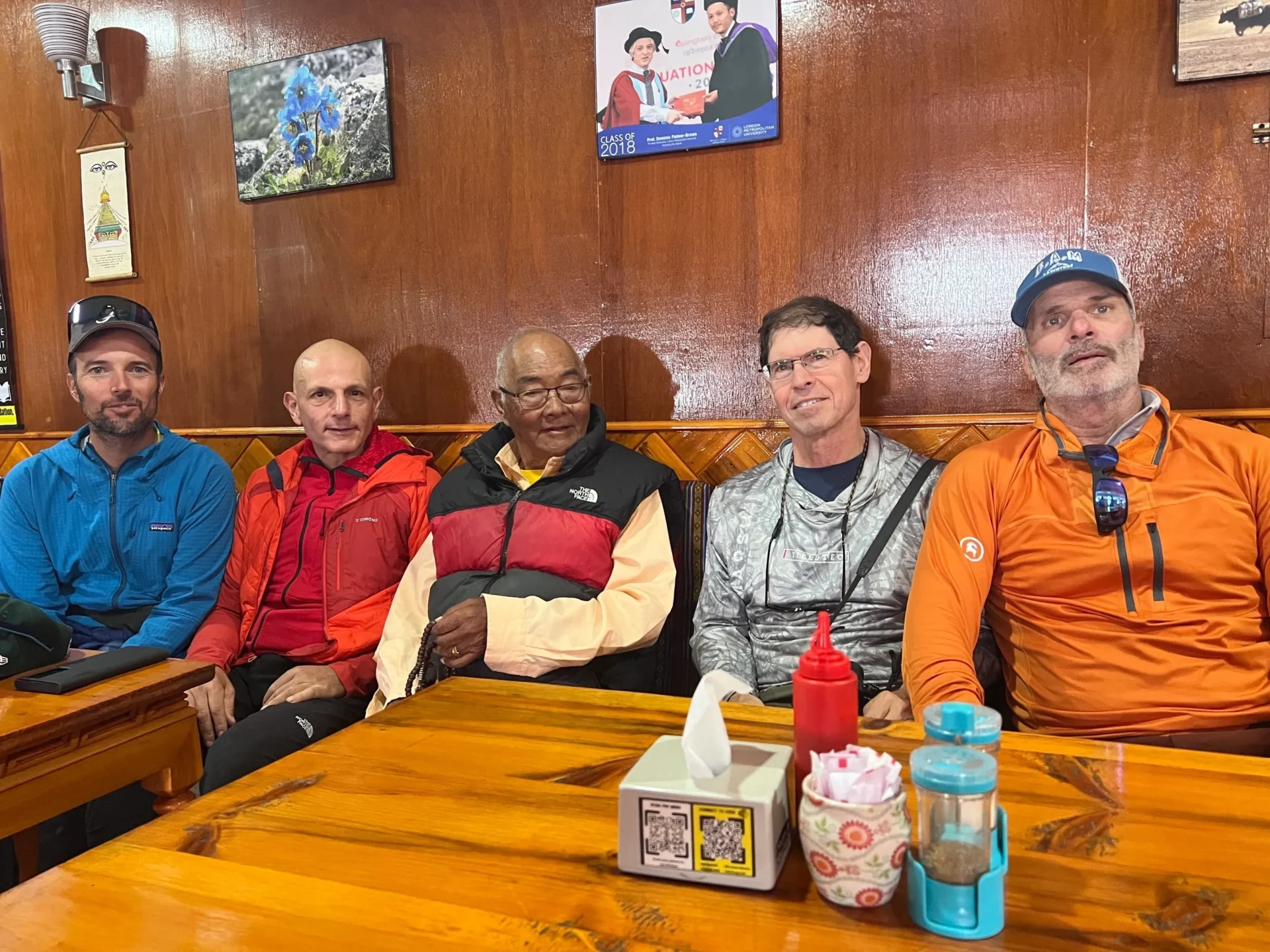 Group of skiers posing on a snowy mountain with lake and peaks behind.