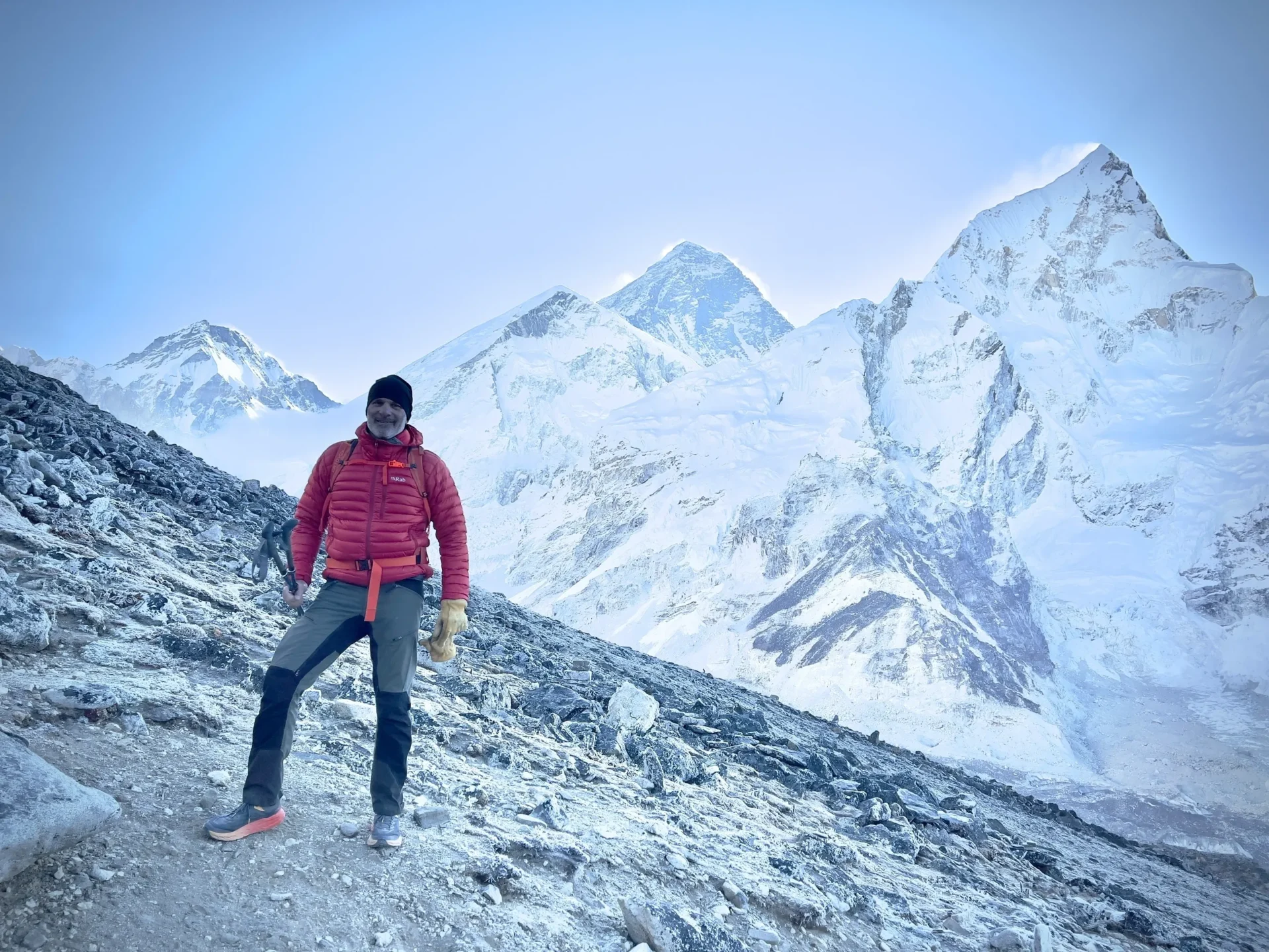 Man in red jacket hiking in snowy mountain terrain with towering peaks in the background.