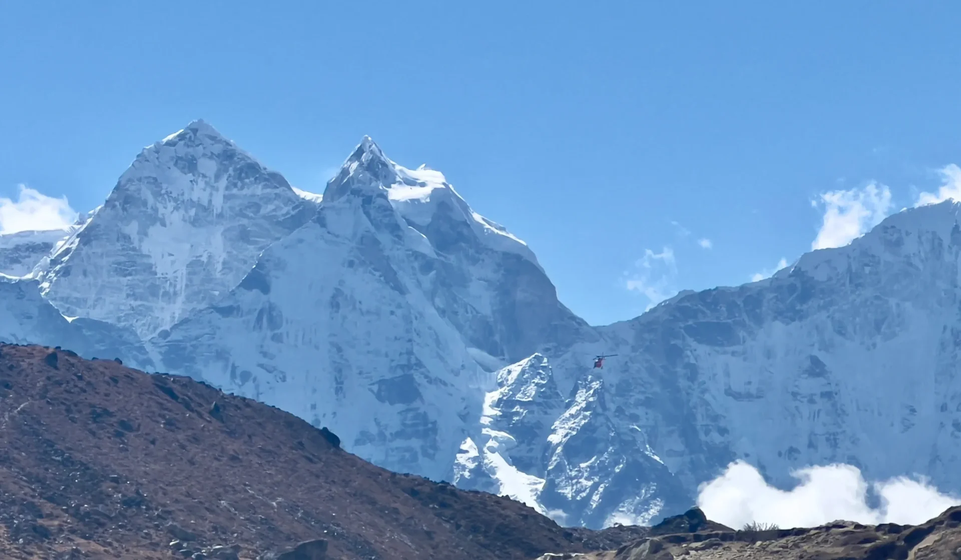 Group of skiers posing on a snowy mountain with lake and peaks behind.