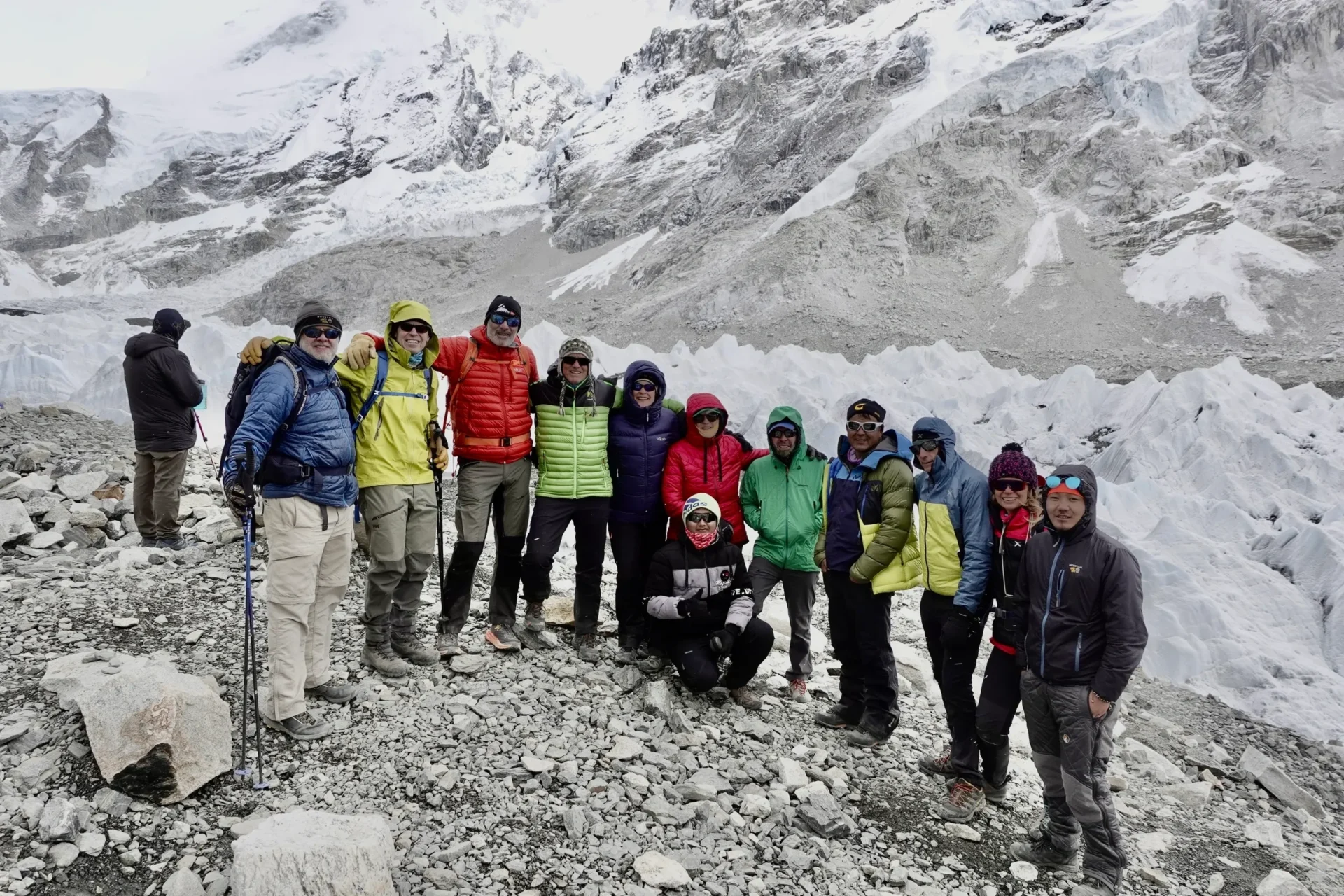 Group of skiers posing on a snowy mountain with lake and peaks behind.