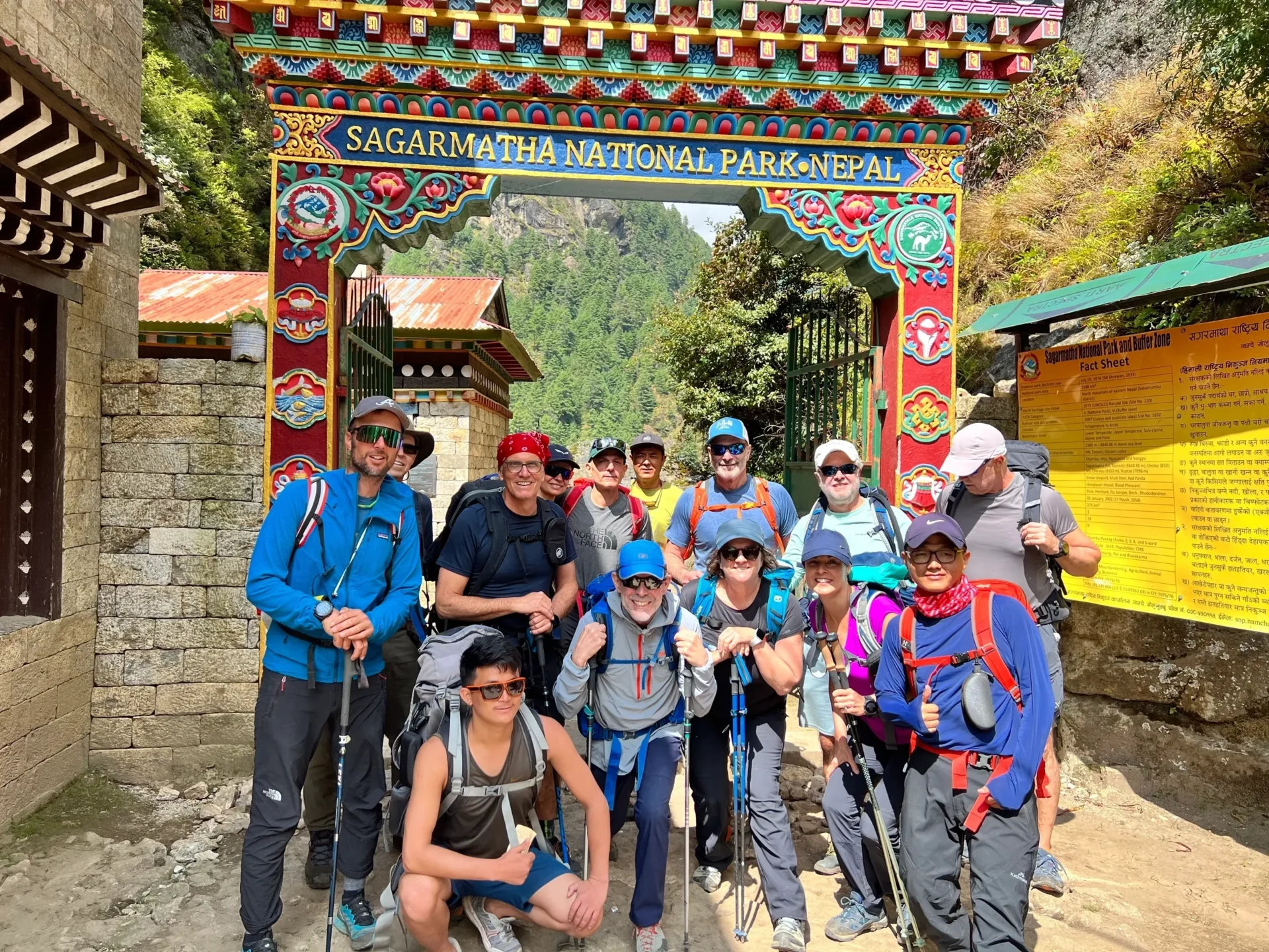 Group of skiers posing on a snowy mountain with lake and peaks behind.