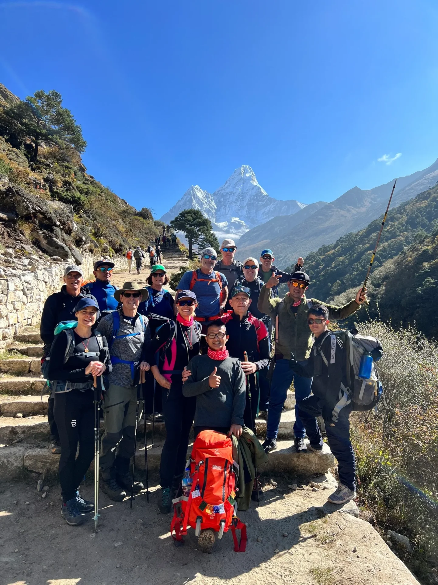 Group of skiers posing on a snowy mountain with lake and peaks behind.