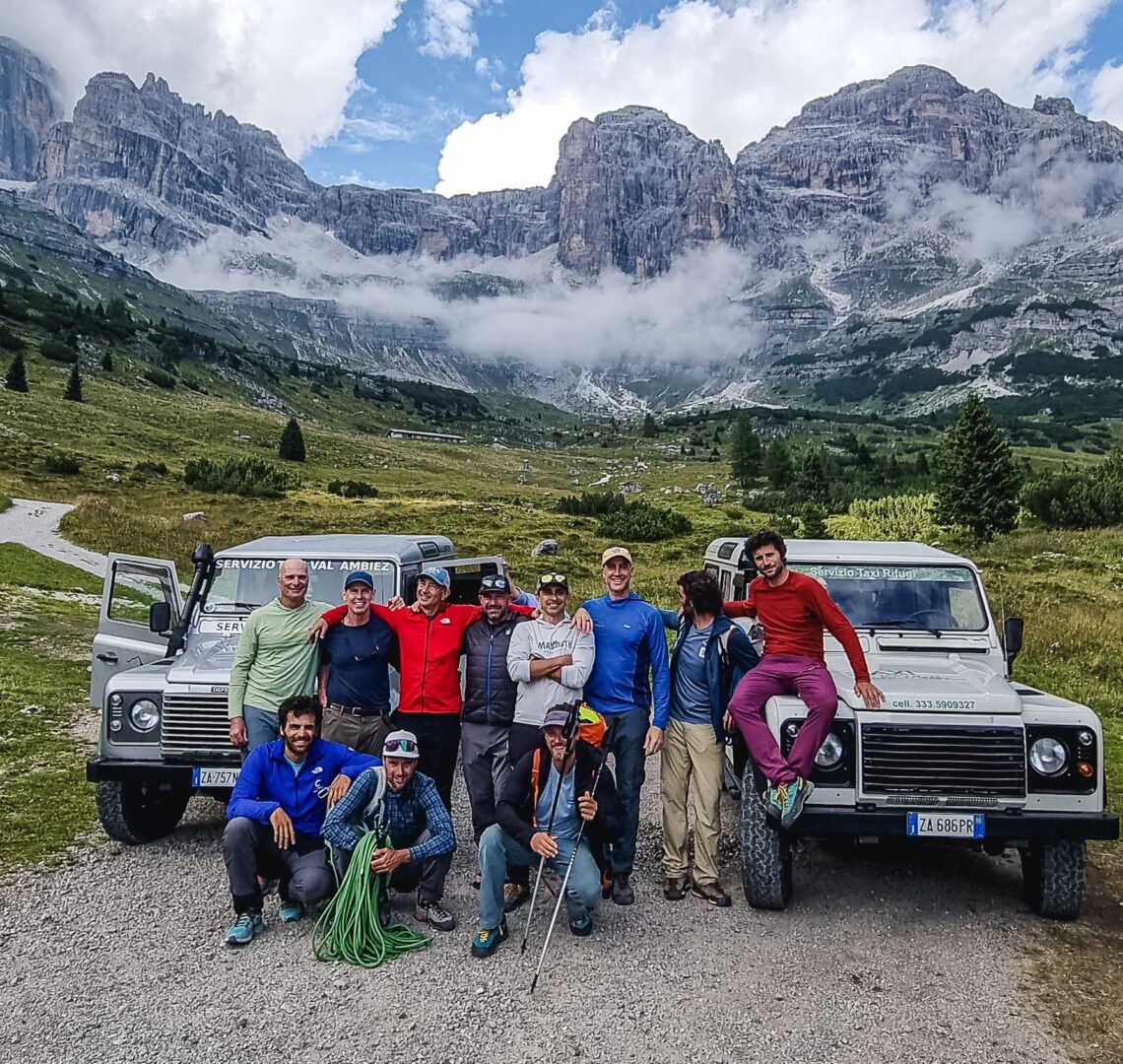 Group of hikers posing with two off-road vehicles in a mountainous landscape.