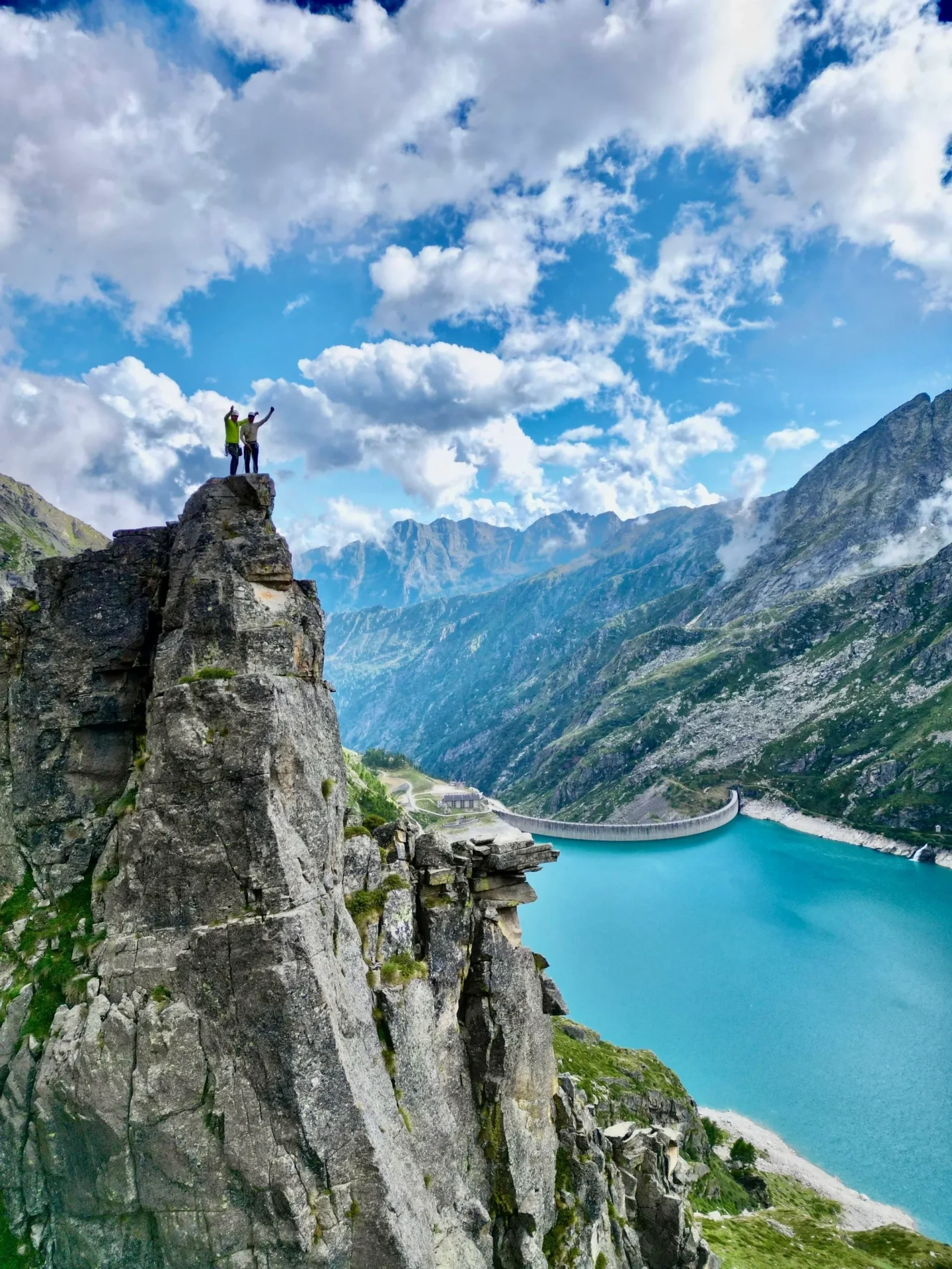 Group of skiers posing on a snowy mountain with lake and peaks behind.