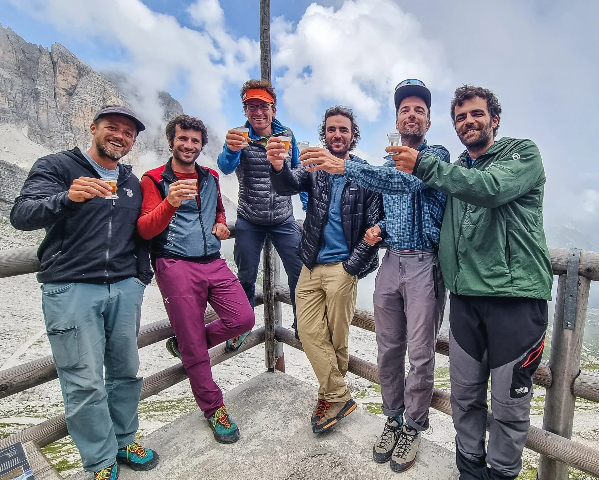 Group of skiers posing on a snowy mountain with lake and peaks behind.