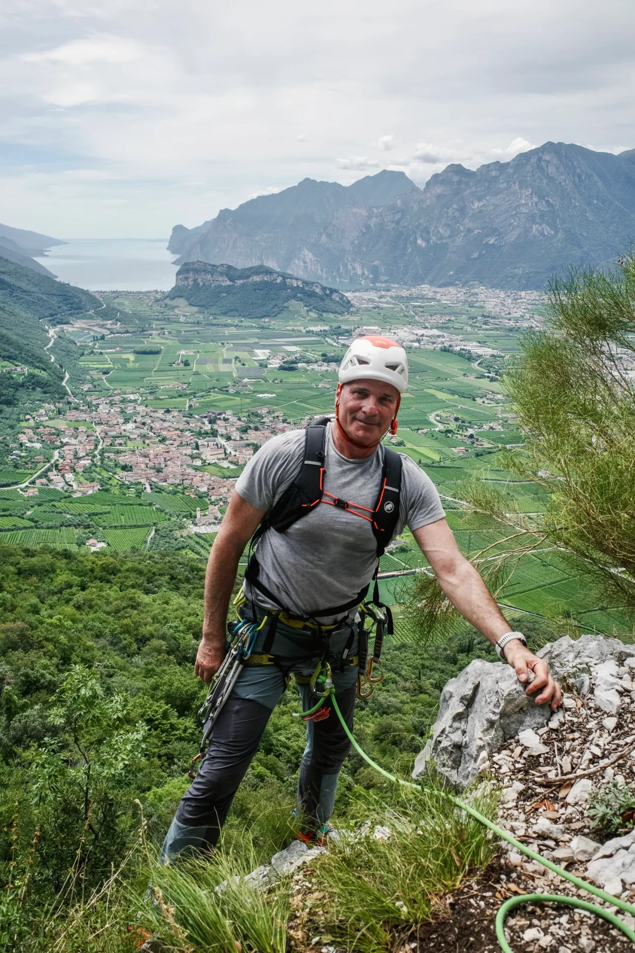 Man climbing a mountain with safety gear overlooking a valley and mountains.