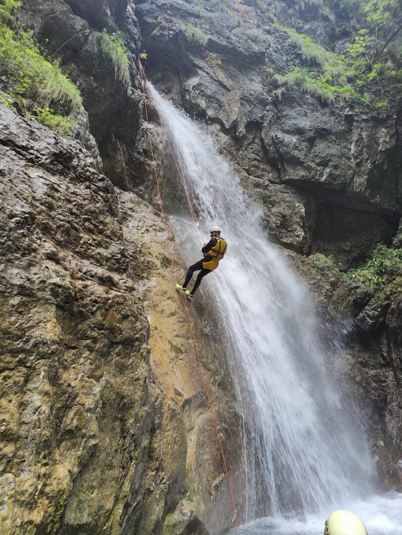 Group of skiers posing on a snowy mountain with lake and peaks behind.
