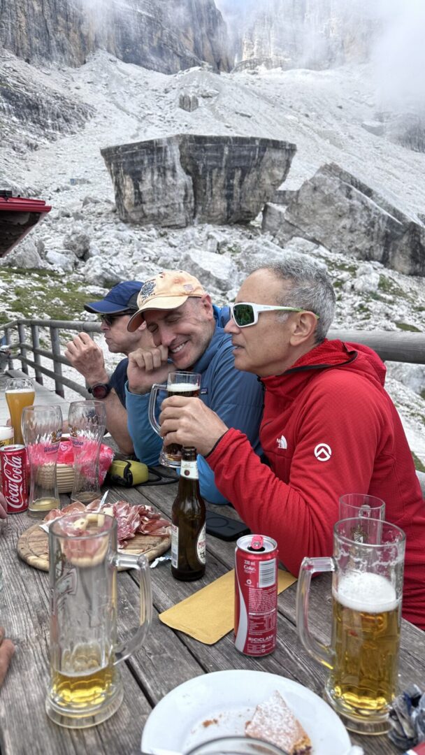 Group of skiers posing on a snowy mountain with lake and peaks behind.