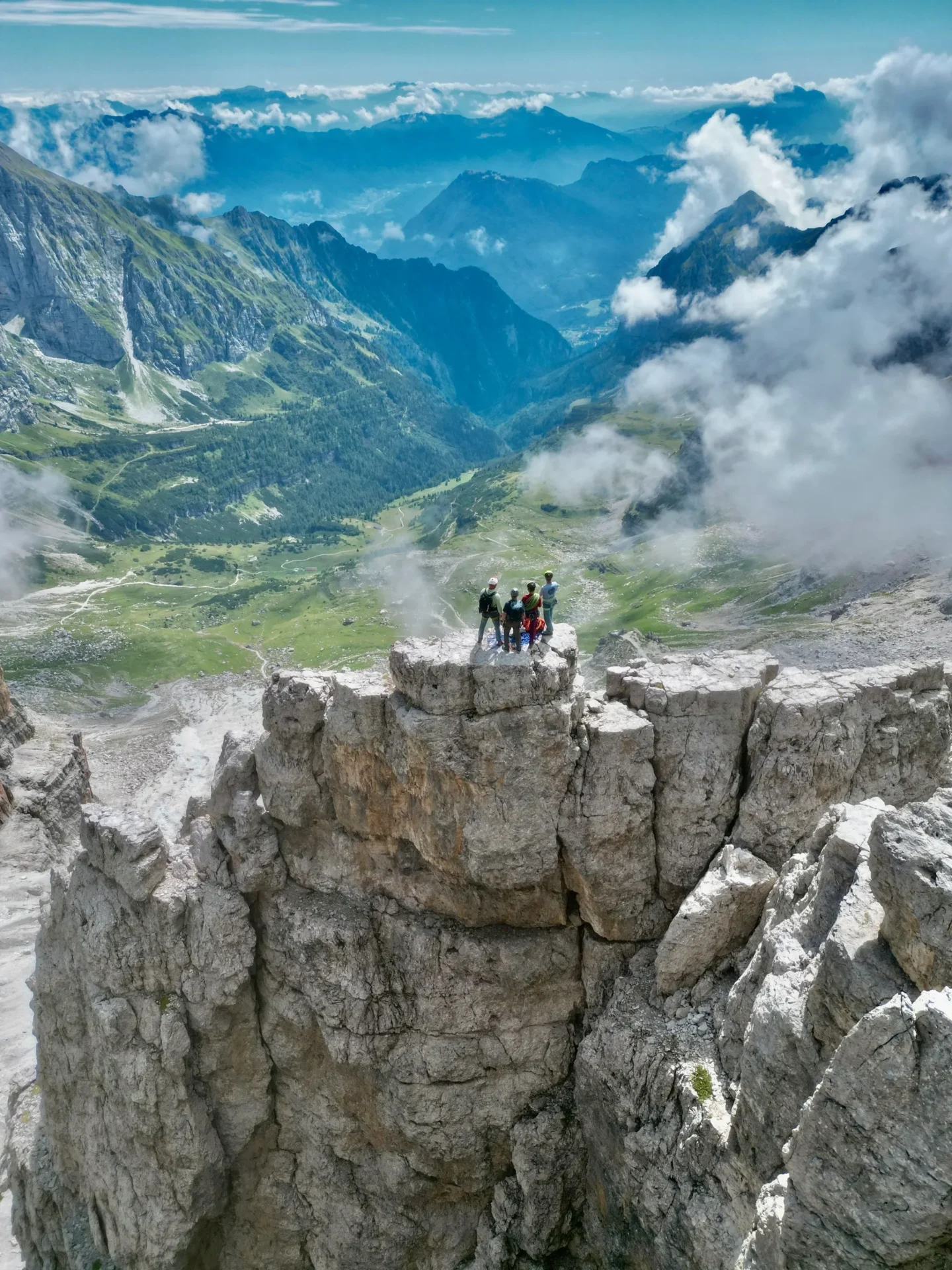 Group of skiers posing on a snowy mountain with lake and peaks behind.
