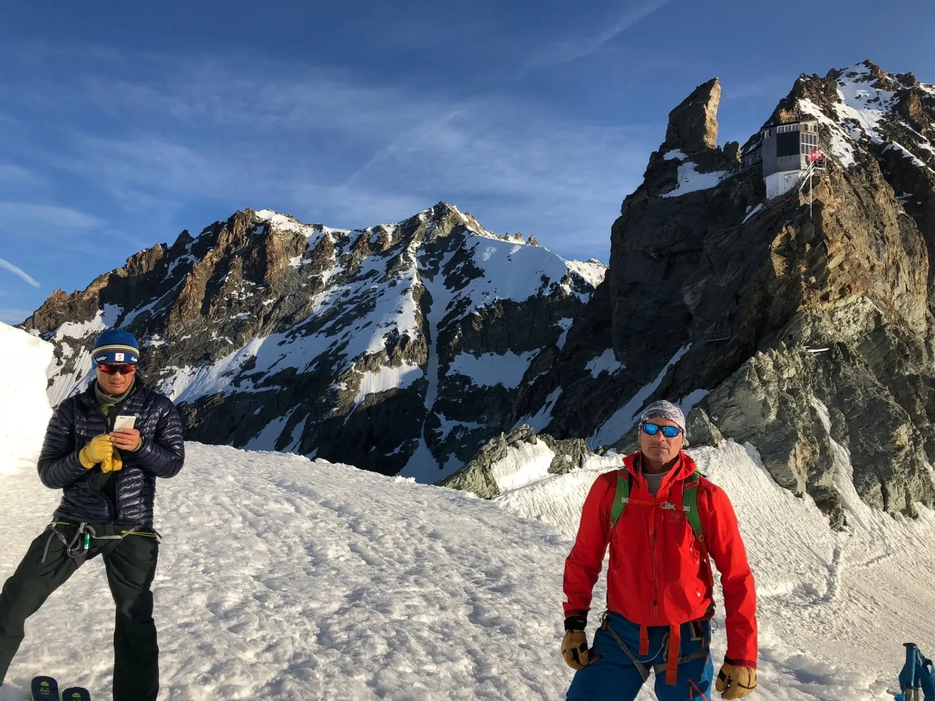 Group of skiers posing on a snowy mountain with lake and peaks behind.