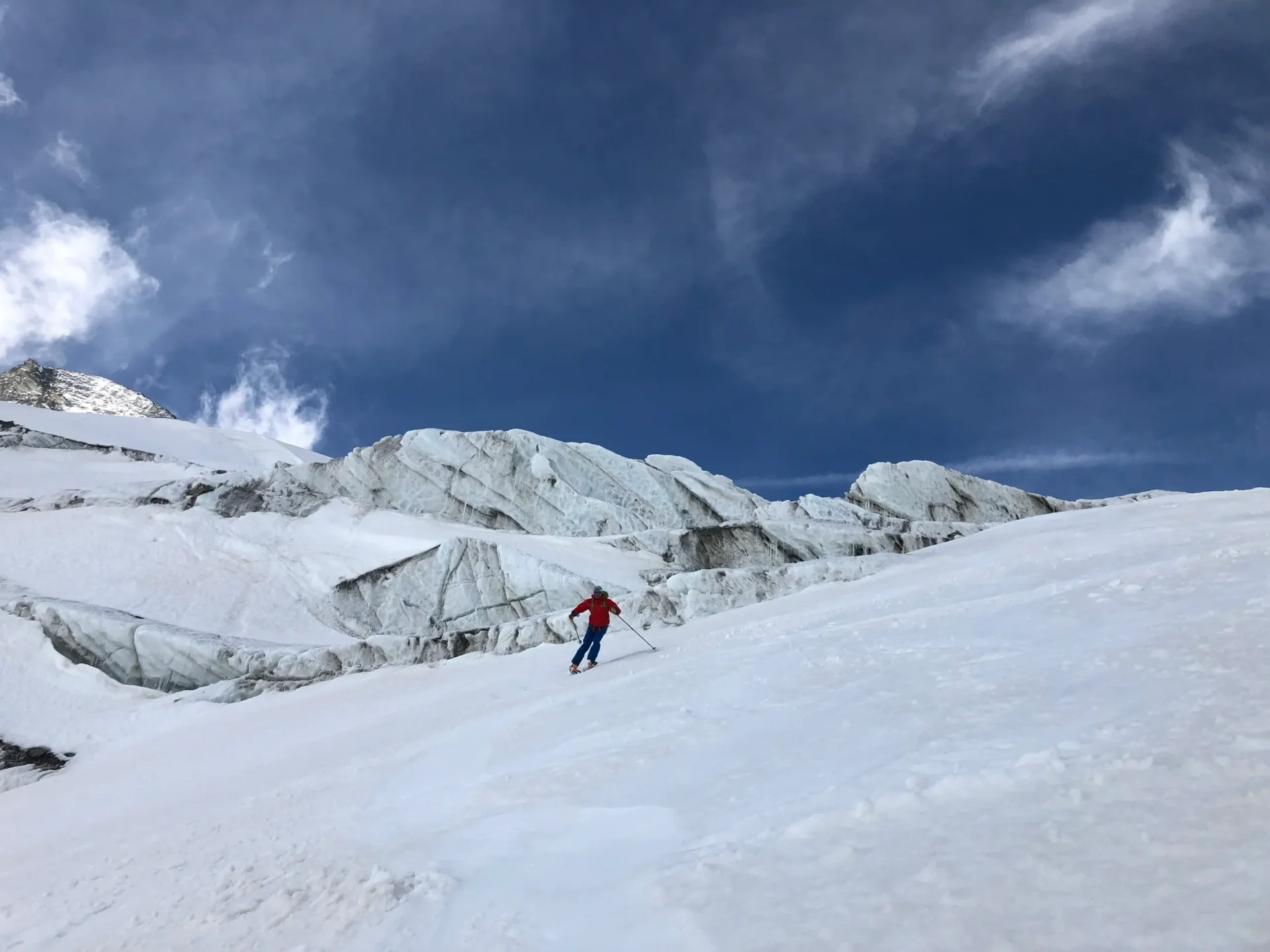 Group of skiers posing on a snowy mountain with lake and peaks behind.