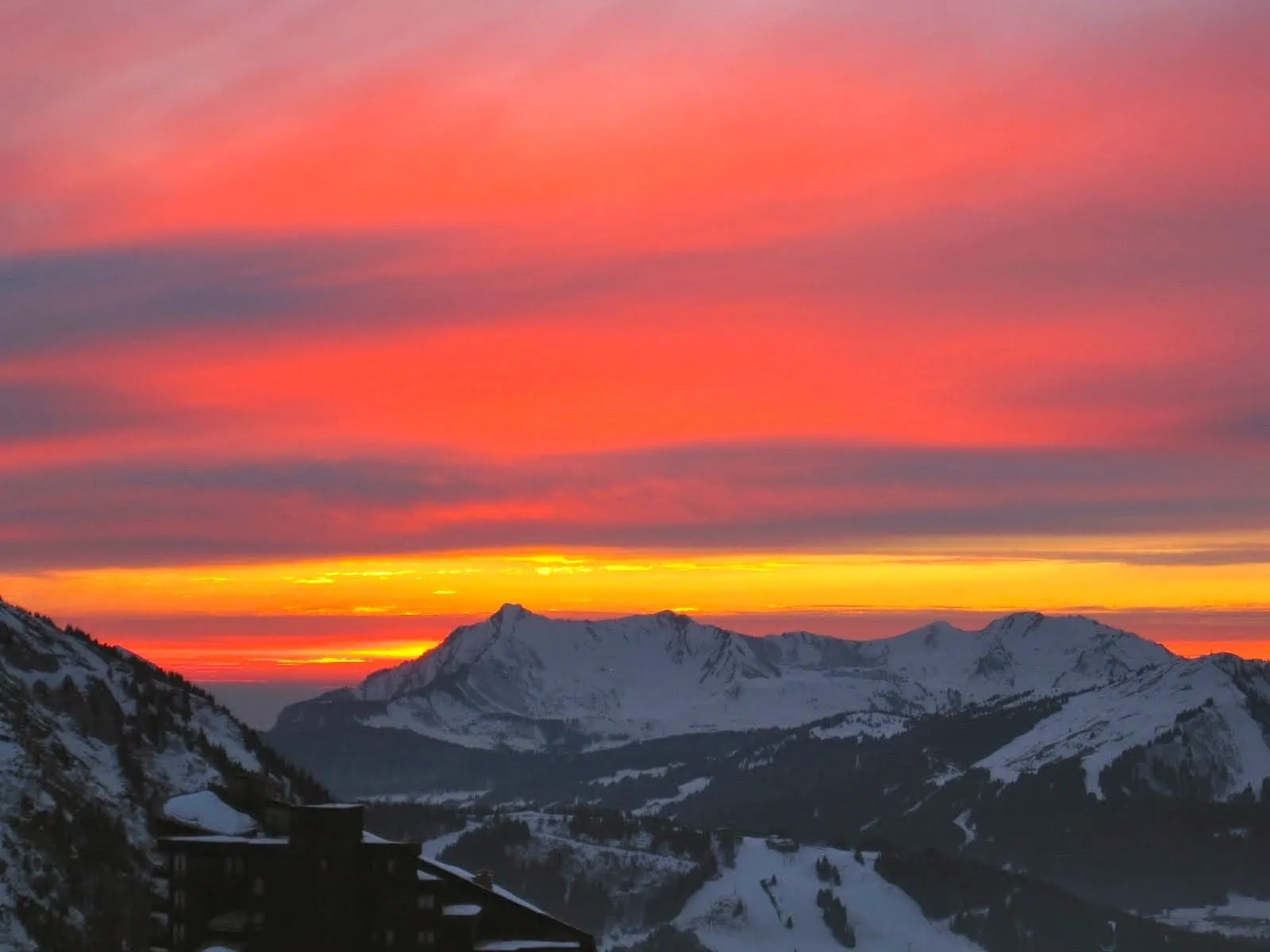 Group of skiers posing on a snowy mountain with lake and peaks behind.