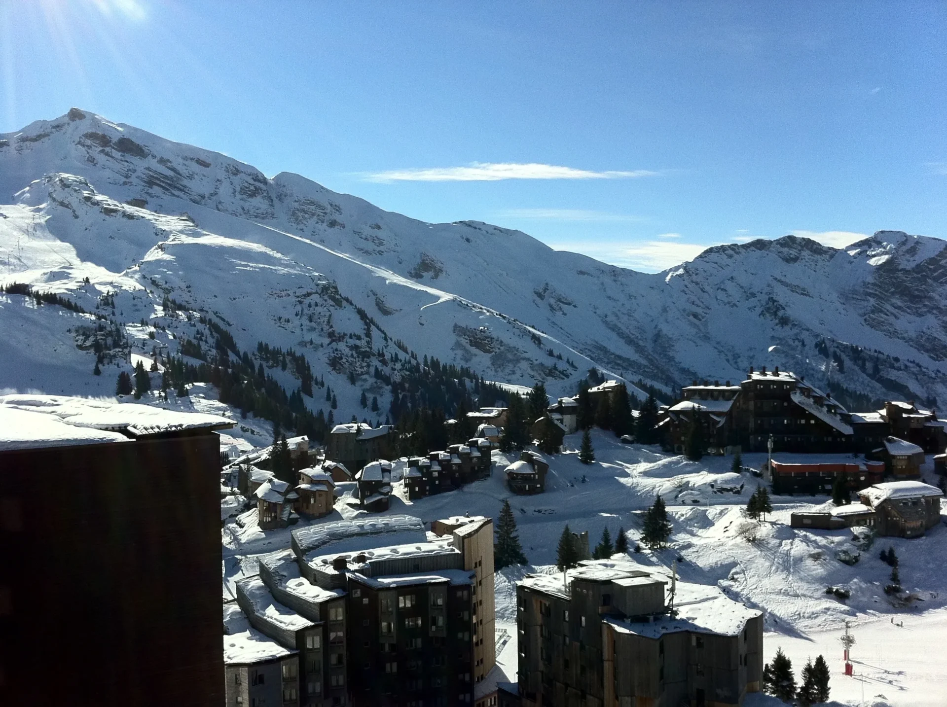 Group of skiers posing on a snowy mountain with lake and peaks behind.