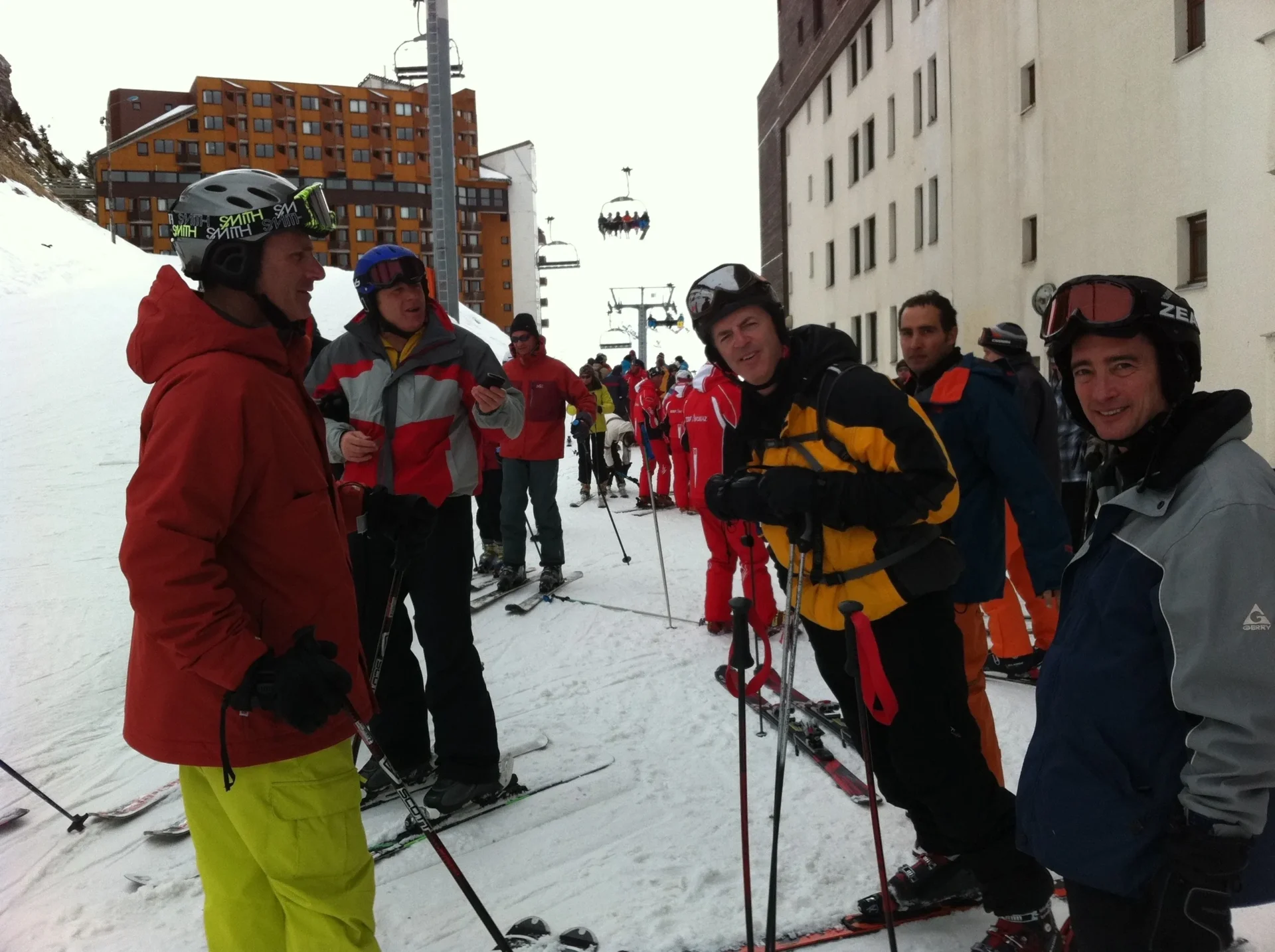Group of skiers posing on a snowy mountain with lake and peaks behind.