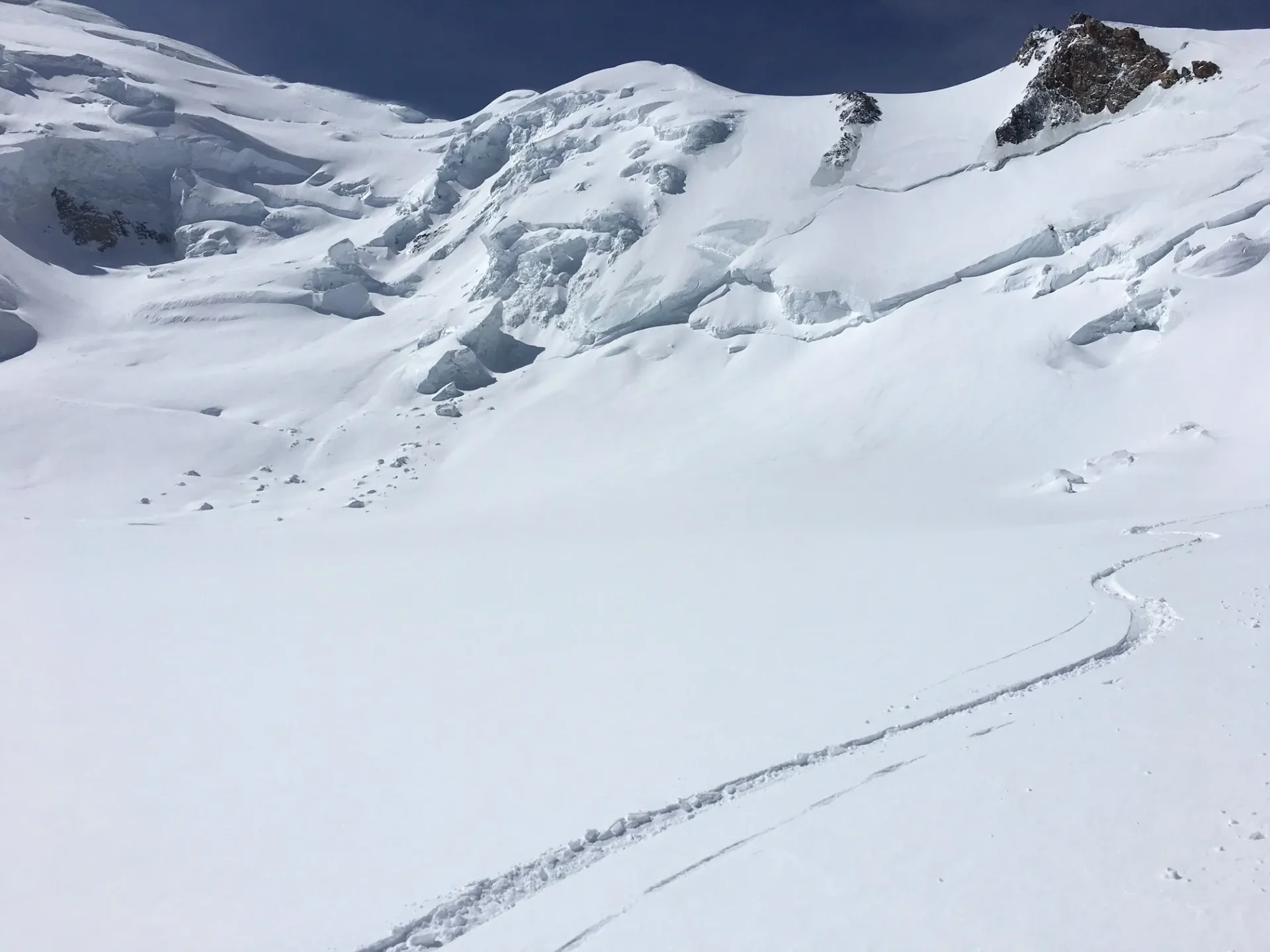 Group of skiers posing on a snowy mountain with lake and peaks behind.