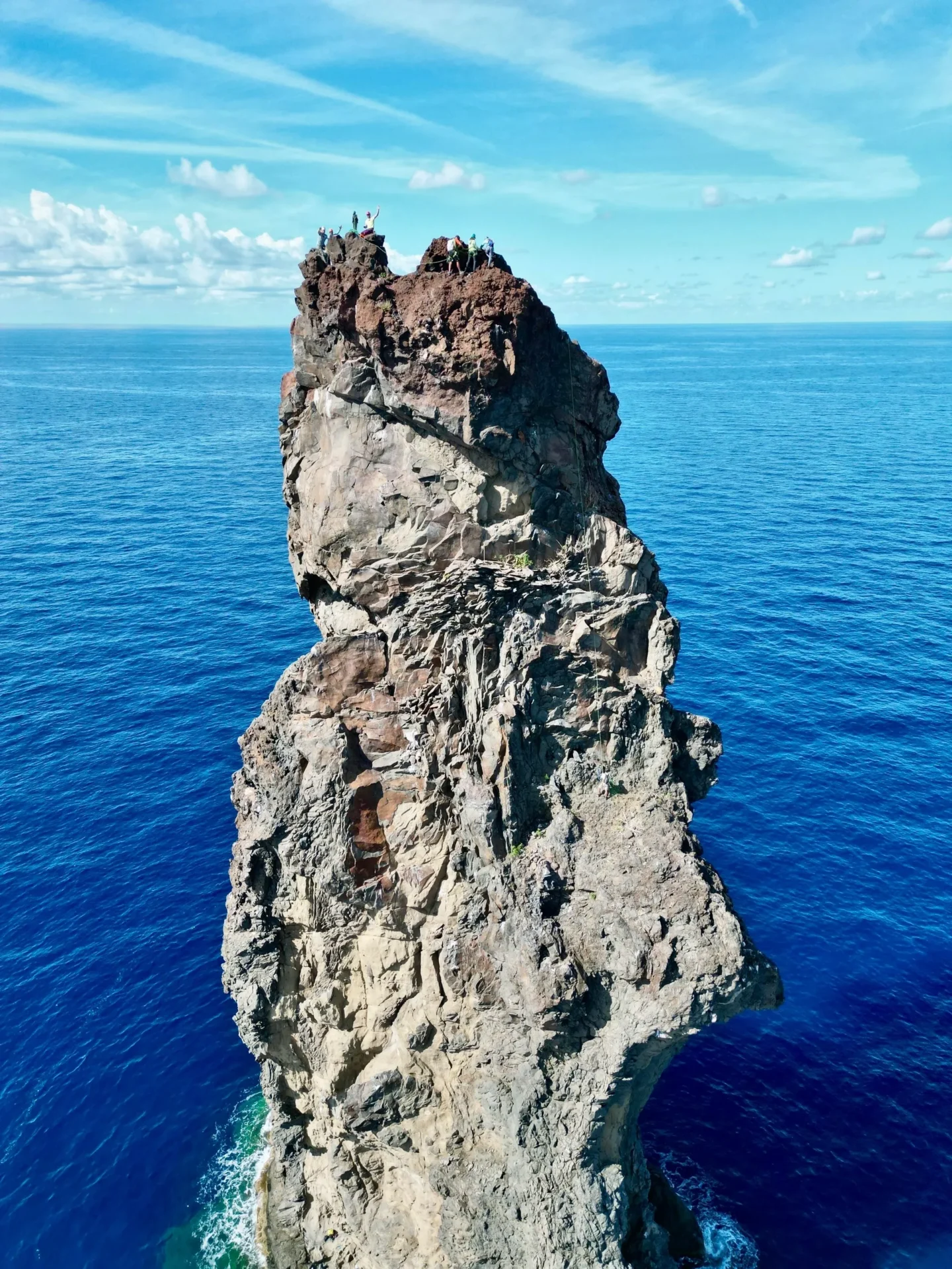 Group of skiers posing on a snowy mountain with lake and peaks behind.