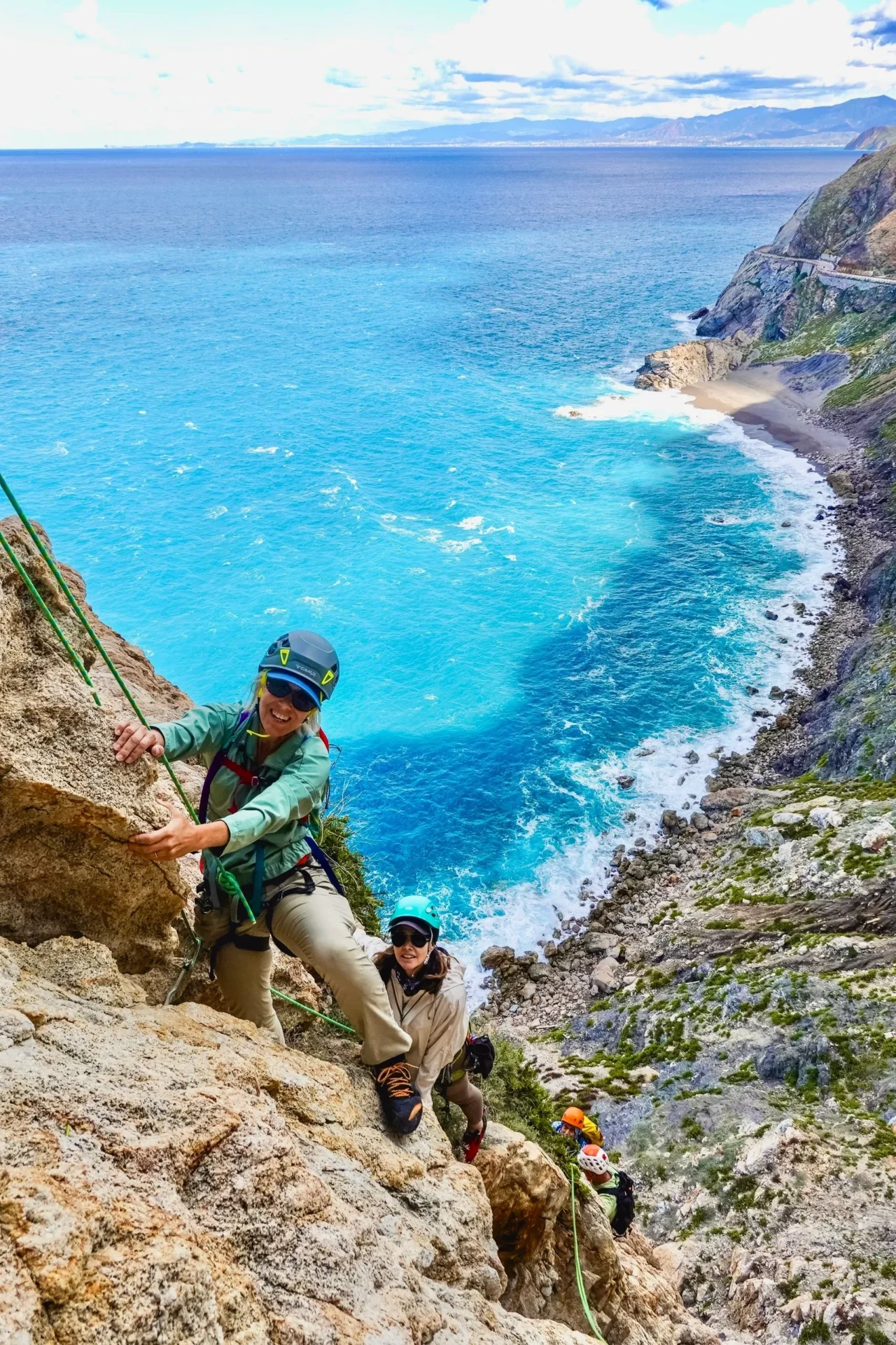 Group of skiers posing on a snowy mountain with lake and peaks behind.