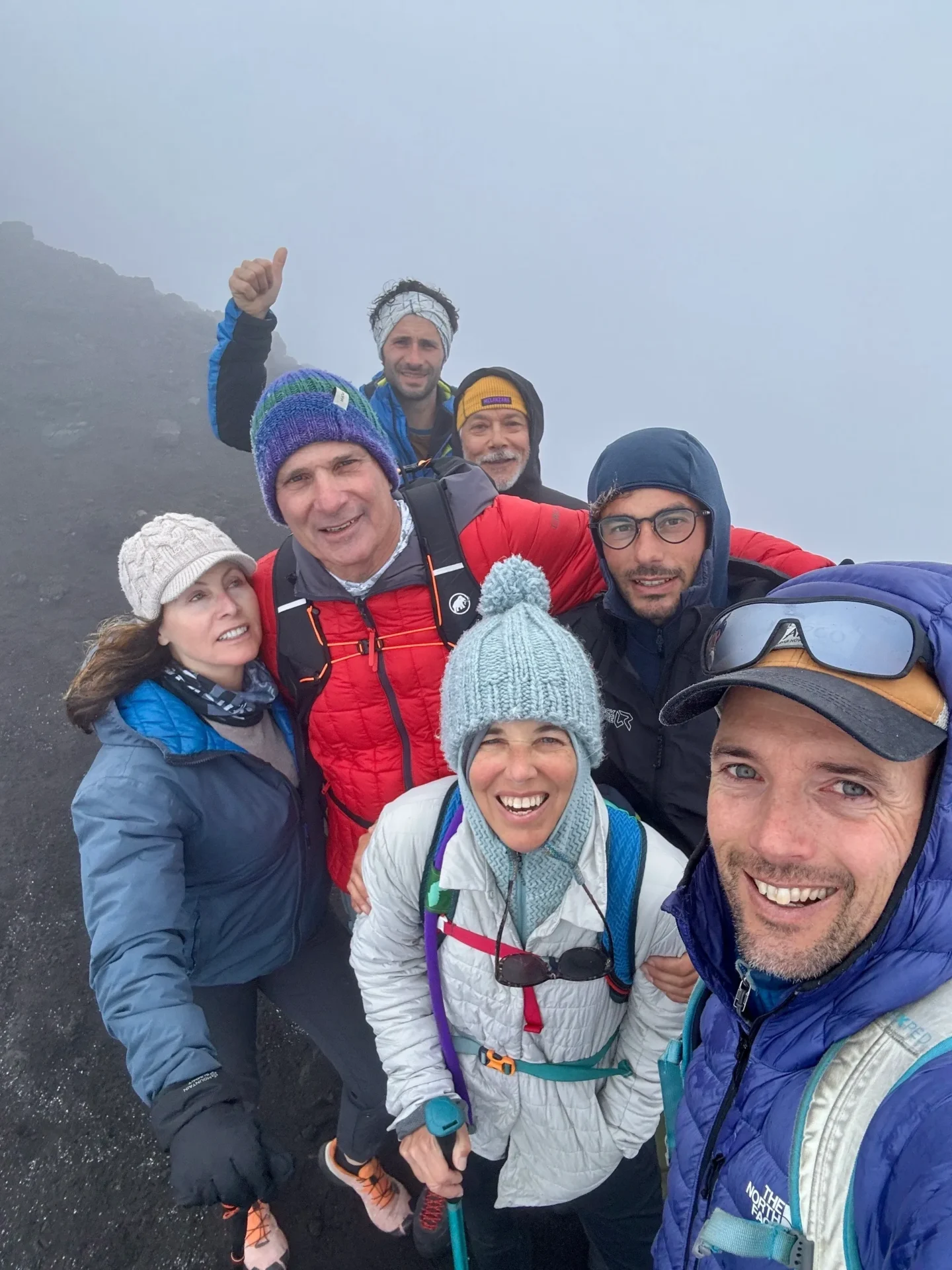 Group of skiers posing on a snowy mountain with lake and peaks behind.