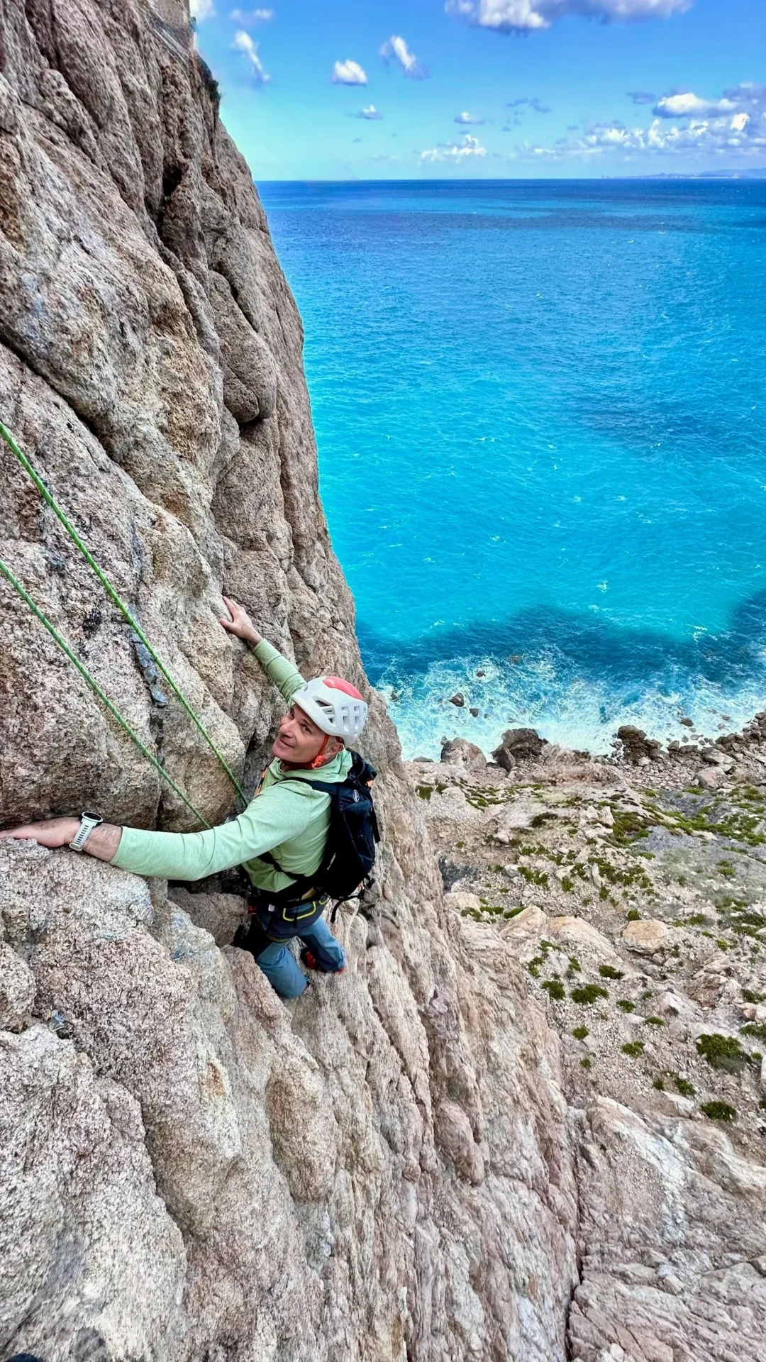 Group of skiers posing on a snowy mountain with lake and peaks behind.